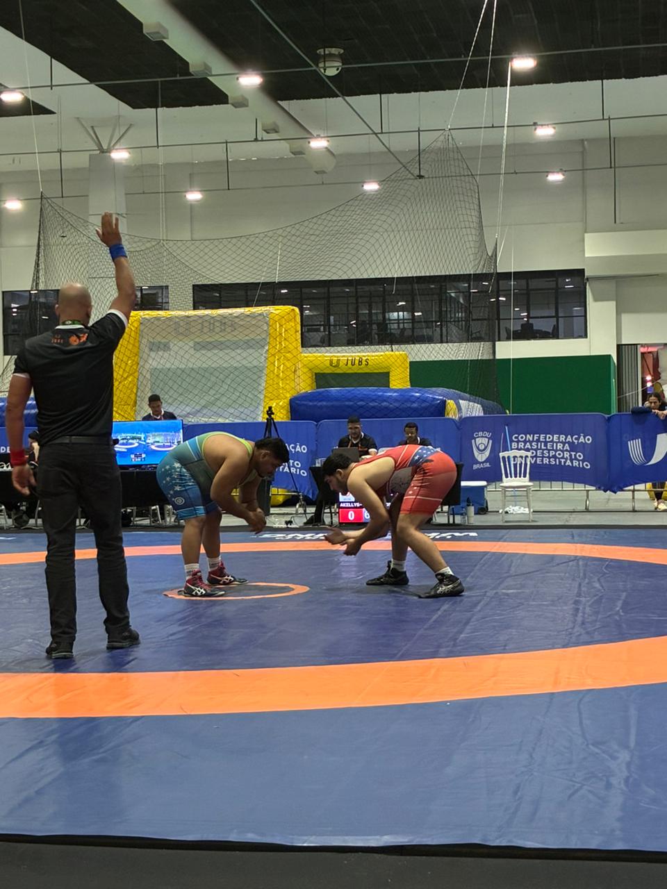 Árbitro sinaliza o início do combate entre Akilys Durval e o adversário no tapete de wrestling dos JUBs